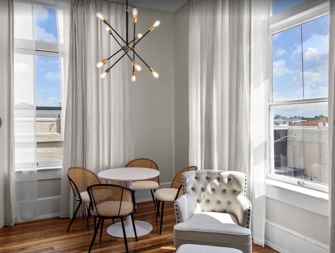 A bright studio corner at The West Main — a tulip table, cane chairs and a sputnik chandelier by tall windows