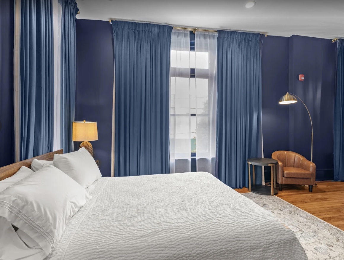 A suite bedroom at The West Main — deep blue walls, crisp white bedding and an arc lamp in the corner